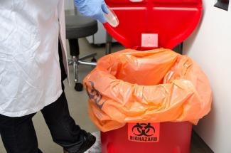 Person throwing away waste into biohazard bin